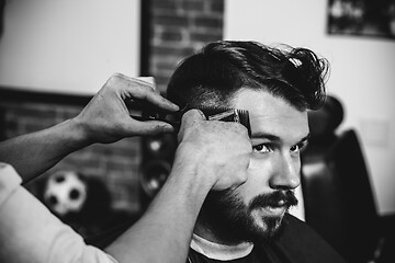 Image showing Young handsome barber making haircut for attractive man in barbershop