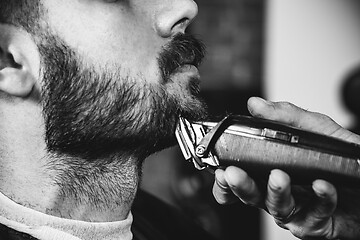 Image showing Young handsome barber making haircut for attractive man in barbershop