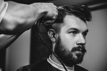 Image showing Young handsome barber making haircut for attractive man in barbershop