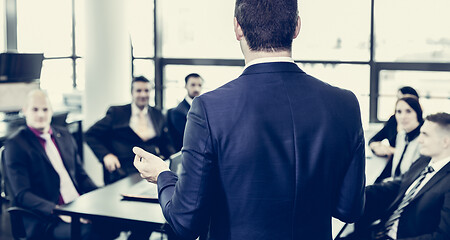 Image showing Successful team leader and business owner leading informal in-house business meeting. Businessman working on laptop in foreground. Business and entrepreneurship concept