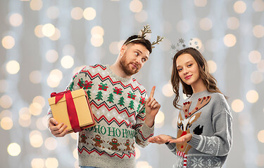 Image showing happy couple in ugly sweaters with christmas gift