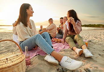 Image showing happy friends eating sandwiches at picnic on beach