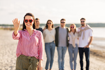 Image showing woman with friends on beach in summer waving hand