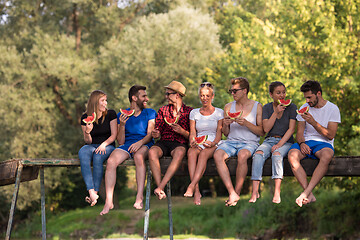 Image showing friends enjoying watermelon while sitting on the wooden bridge