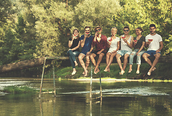 Image showing friends enjoying watermelon while sitting on the wooden bridge