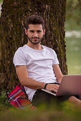 Image showing man using a laptop computer on the bank of the river