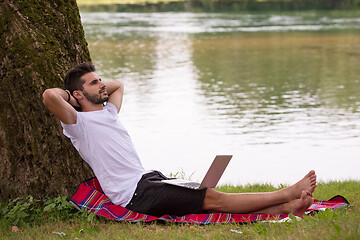 Image showing man using a laptop computer on the bank of the river