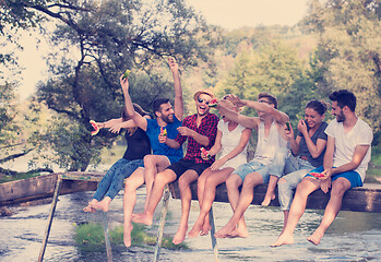 Image showing friends enjoying watermelon while sitting on the wooden bridge