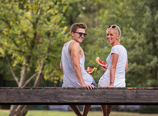 Image showing couple enjoying watermelon while sitting on the wooden bridge