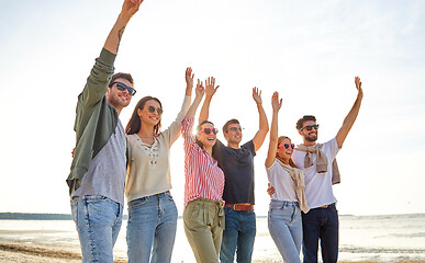 Image showing happy friends waving hands on beach in summer