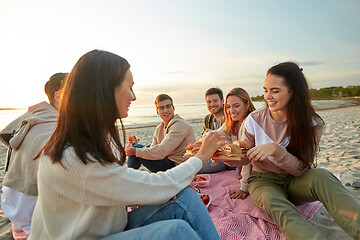 Image showing happy friends eating sandwiches at picnic on beach