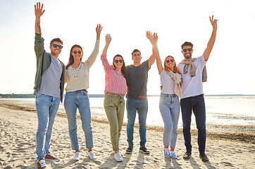 Image showing happy friends waving hands on beach in summer