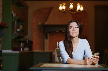 Image showing Smiling woman sitting and table and using smartphone