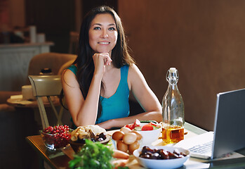 Image showing Woman eating healthy food at the table with laptop