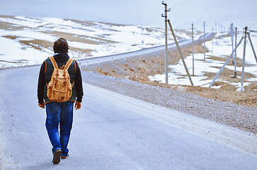 Image showing Traveller wearing backpack and walking along rural highway