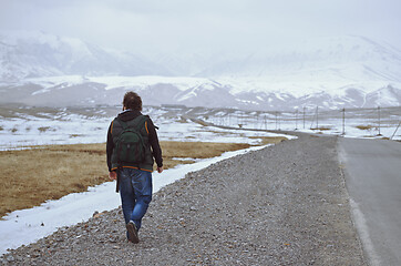 Image showing Traveller wearing backpack and walking along rural highway