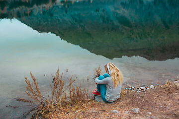 Image showing Woman listening music at the water's edge of mountain lake