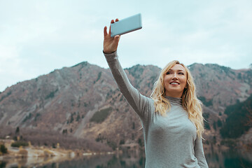 Image showing Smiling woman makes selfie at the mountain lake