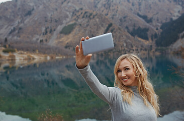 Image showing Smiling woman makes selfie at the mountain lake