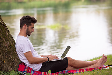 Image showing man using a laptop computer on the bank of the river