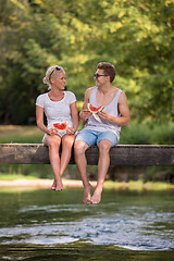 Image showing couple enjoying watermelon while sitting on the wooden bridge