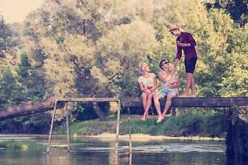 Image showing friends enjoying watermelon while sitting on the wooden bridge