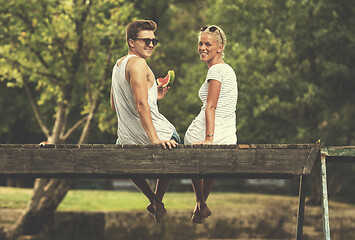 Image showing couple enjoying watermelon while sitting on the wooden bridge