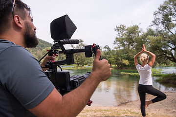 Image showing young videographer recording while woman doing yoga exercise