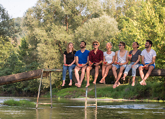 Image showing friends enjoying watermelon while sitting on the wooden bridge