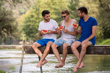 Image showing men enjoying watermelon while sitting on the wooden bridge