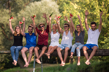 Image showing friends enjoying watermelon while sitting on the wooden bridge