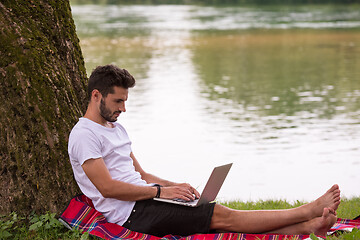 Image showing man using a laptop computer on the bank of the river