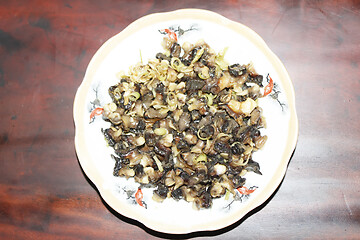 Image showing Closeup of eating the fried snails with stalks lemon grass 