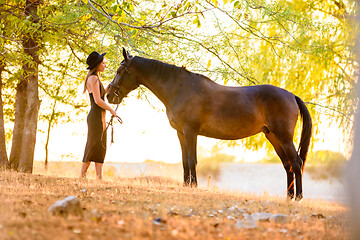 Image showing Beautiful girl stands with a horse in the forest at sunset with beautiful backlighting