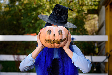 Image showing A girl dressed as a witch covered her face with a pumpkin with an evil face drawn in the style of a Halloween celebration