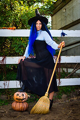 Image showing Cute girl in a witch costume with pumpkins and a broom