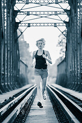 Image showing Athlete running on railaway bridge training for marathon and fitness. Healthy sporty caucasian woman exercising in urban environment before going to work. Active urban lifestyle