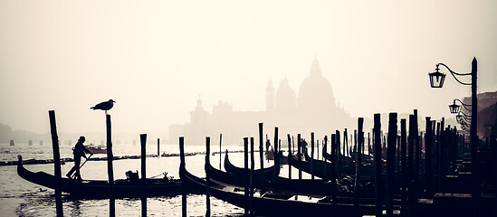 Image showing Romantic Italian city of Venice, a World Heritage Site: traditional Venetian wooden boats, gondolier and Roman Catholic church Basilica di Santa Maria della Salute in the misty background