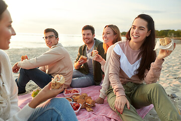 Image showing happy friends eating sandwiches at picnic on beach