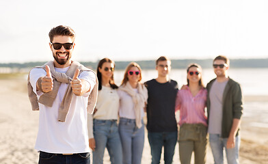 Image showing happy man with friends on beach showing thumbs up