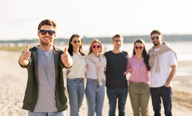 Image showing happy man with friends on beach showing thumbs up