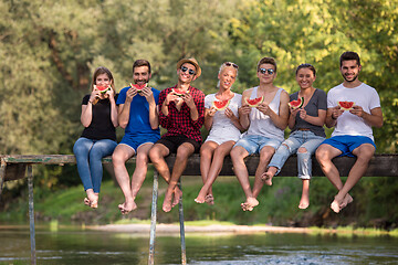 Image showing friends enjoying watermelon while sitting on the wooden bridge