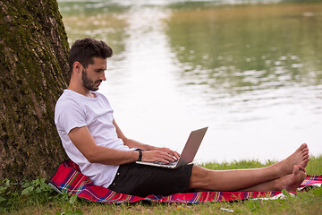 Image showing man using a laptop computer on the bank of the river