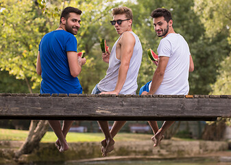 Image showing men enjoying watermelon while sitting on the wooden bridge