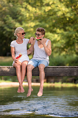 Image showing couple enjoying watermelon while sitting on the wooden bridge