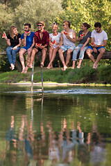 Image showing friends enjoying watermelon while sitting on the wooden bridge