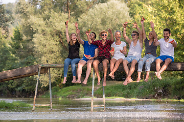 Image showing friends enjoying watermelon while sitting on the wooden bridge