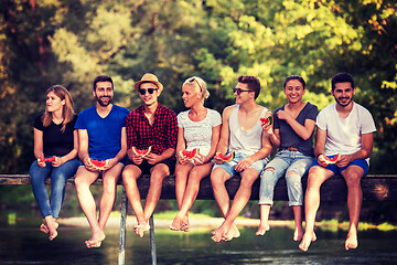 Image showing friends enjoying watermelon while sitting on the wooden bridge