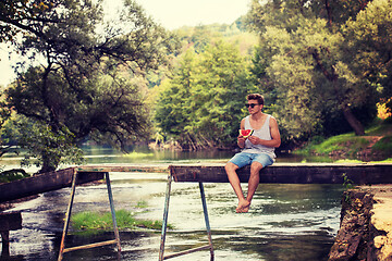 Image showing man enjoying watermelon while sitting on the wooden bridge