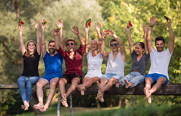 Image showing friends enjoying watermelon while sitting on the wooden bridge